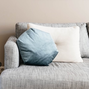 May include: A gray sofa with a blue and white pillow, a black side table with a green glass vase and a green glass lamp, and a wooden floor.