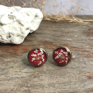 Könnte beinhalten: Ein Paar rote Ohrstecker mit einer zarten weißen Blume, die in jeden Ohrstecker gepresst ist. Die Ohrringe haben eine Messingfassung.