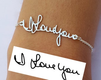 May include: A silver-toned metal bracelet featuring a cursive script design that reads I Love You. The bracelet is attached to a delicate chain and is displayed on a wrist. Below the bracelet, a white rectangular card displays the text I Love You.
