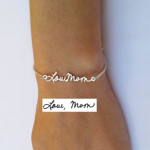 May include: A silver bracelet with the handwritten inscription "Love, Mom" is displayed on a wrist. The bracelet's delicate chain supports the cursive text. A rectangular image below the bracelet also displays the text "Love, Mom".
