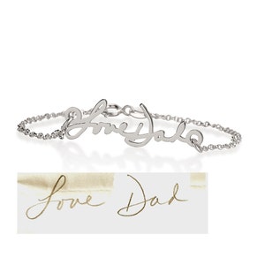 May include: A silver-colored metal bracelet featuring a cursive script pendant that reads Love Dad. The pendant is attached to a delicate chain with a circular clasp. Below the bracelet is a sample of the handwritten text Love Dad in gold ink.