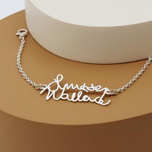 May include: A silver-toned metal bracelet featuring a central nameplate with the cursive script text "Smyser Wallace". The bracelet is constructed with a delicate chain link design and includes a small lobster claw clasp at one end of the chain.