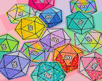 May include: A collection of 13 iridescent glitter dice stickers with a black outline and the number 20 printed on each die. The stickers are arranged on a pink and green checkered background.