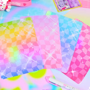 May include: Four iridescent holographic cards with a checkered pattern and a rainbow gradient. The cards have a glittery effect and are arranged in a fan shape.