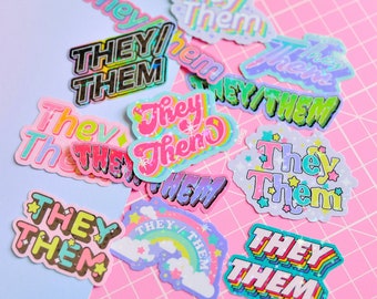 May include: A collection of colorful stickers with the text "They/Them" in various fonts and designs. The stickers are on a pink and blue background.