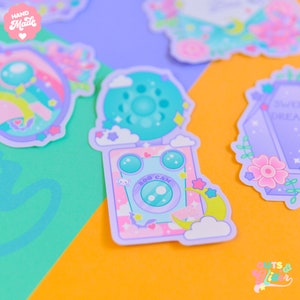 Op de afbeelding: Een pastelkleurige sticker in paars en roze met een cartooncamera met een hartje, een spin en de tekst "BOO CAM". De camera wordt omringd door wolken, sterren en een halve maan. De sticker maakt deel uit van een set stickers met een grillig, griezelig thema.