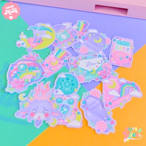 Op de afbeelding: Een set van 10 pastelkleurige stickers met verschillende schattige illustraties. De stickers bevatten een regenboog, een halve maan, een kattenpoot, een hart, een kist, een brief, een radio en een vuur. De stickers zijn handgemaakt en hebben een speels, magisch thema.