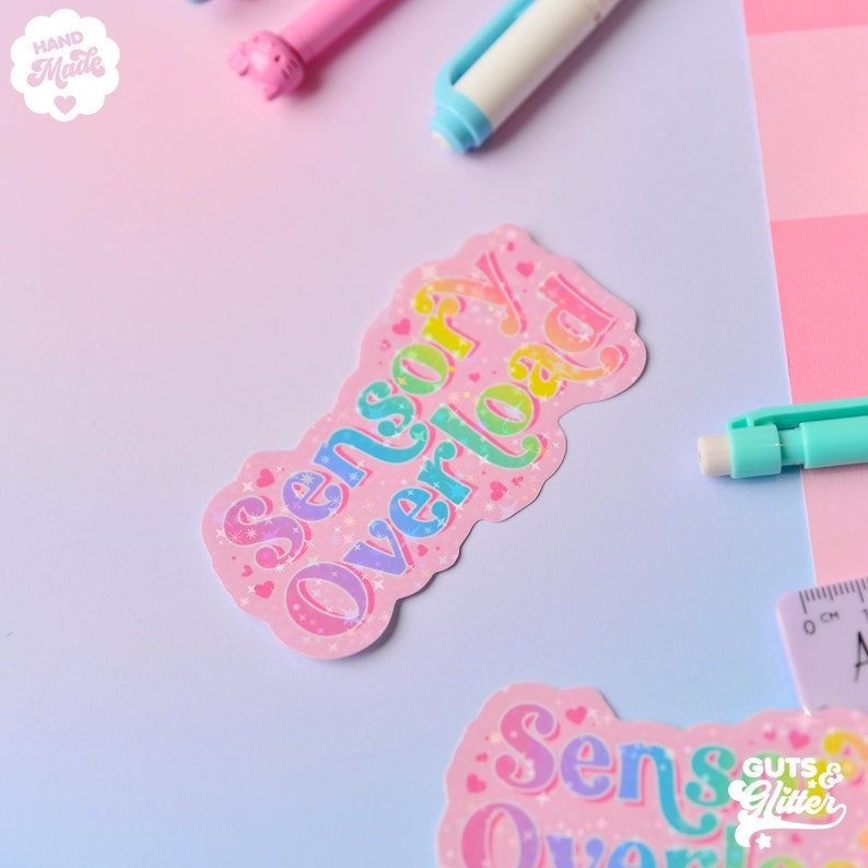 Pu&ograve; includere: Un adesivo rosa con il testo "Sensory Overload" in colori arcobaleno con glitter e stelle. L'adesivo &egrave; su uno sfondo rosa e blu chiaro.