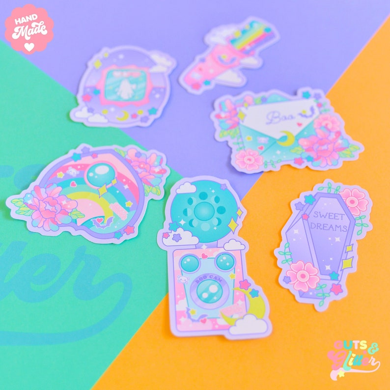 Op de afbeelding: Een set van zes kleurrijke stickers met verschillende schattige ontwerpen, waaronder een regenboog, een camera, een kist, een brief en een ruimteschip. De stickers zijn allemaal met de hand getekend en hebben een speelse, dromerige esthetiek.