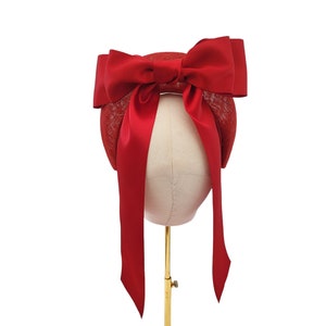 May include: A red hat with a large red satin bow. The hat is on a gold stand.