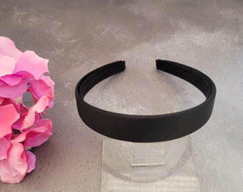 May include: A black headband made of a soft, flexible material. The headband is on a clear display stand.
