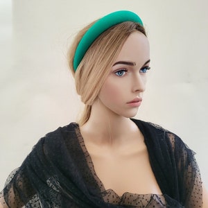 May include: A bright teal headband made of fabric. The headband is wide and has a smooth, rounded shape. It is worn by a mannequin with blonde hair and a black polka dot mesh top.
