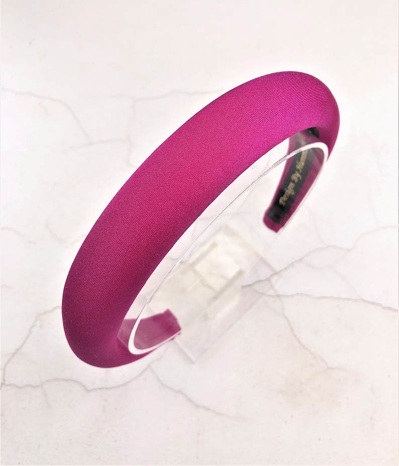 May include: A wide, fuchsia pink satin headband. The headband is made of a soft, smooth fabric and has a simple, elegant design.