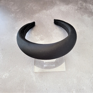 Può includere: Una fascia per capelli nera imbottita con finitura liscia e opaca. L'interno è foderato con un tessuto nero strutturato. La fascia è larga circa 2,5 cm ed è progettata per essere indossata comodamente. Questo accessorio per capelli è adatto a vari tipi di acconciatura.