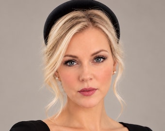 May include: A wide, padded headband crafted from a smooth, solid black velvet fabric. The accessory features a rounded, elevated profile that sits securely atop the head, providing a clean and uniform appearance across the entire surface of the band.