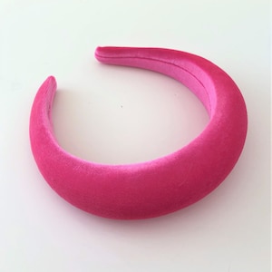 Può includere: Un cerchietto in velluto rosa acceso. Il cerchietto è largo e ha una texture liscia e morbida.