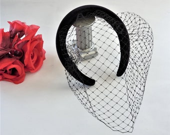 May include: A black velvet headband with a black tulle veil attached. The headband is on a white surface.
