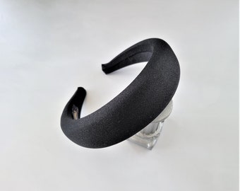 May include: A black padded headband for hair. The headband is thick and wide, and has a smooth, velvety texture.