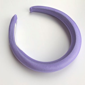 May include: A wide, lavender-colored headband made of soft fabric. The headband is designed to be worn around the head and is a popular accessory for women.