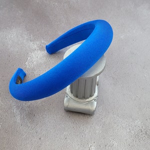 May include: A bright blue headband made of soft fabric. The headband is curved and has a smooth, even surface.