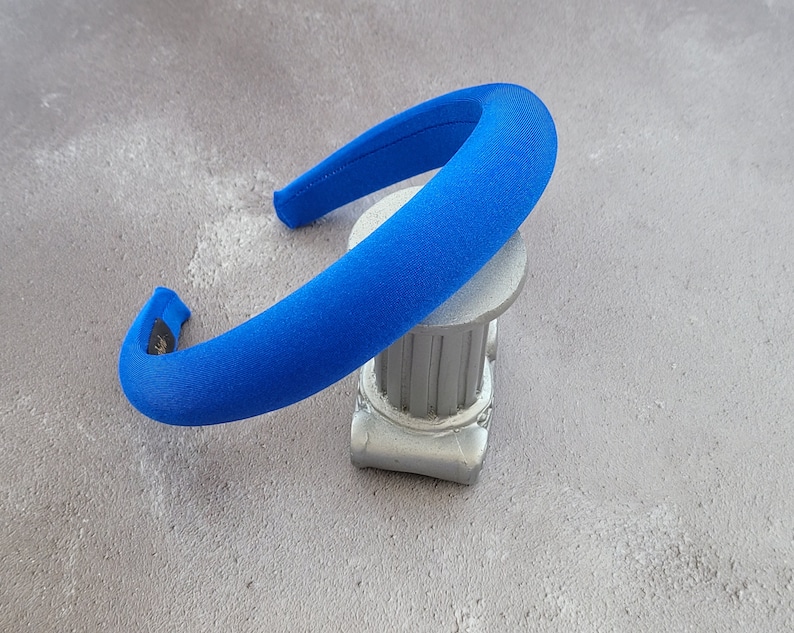 May include: A bright blue headband made of soft fabric. The headband is curved and has a smooth, even surface.