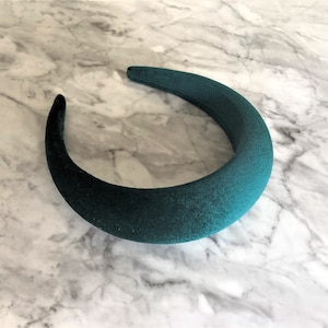 Può includere: Un'ampia fascia per capelli in velluto verde scuro. La fascia è curva e ha una texture liscia e morbida.