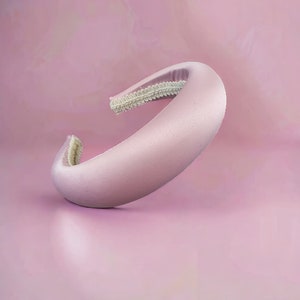 Può includere: Un cerchietto in raso rosa chiaro con un elastico bianco.