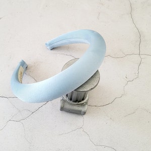 Può includere: Un cerchietto di colore azzurro chiaro realizzato in tessuto morbido. Il cerchietto è curvo e ha una finitura liscia e satinata.