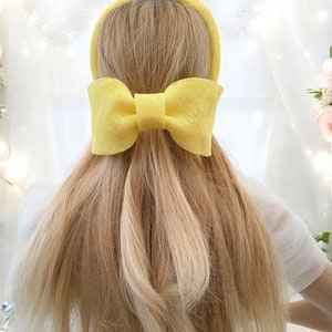 May include: A yellow headband with a large yellow bow. The headband is made of a woven material.