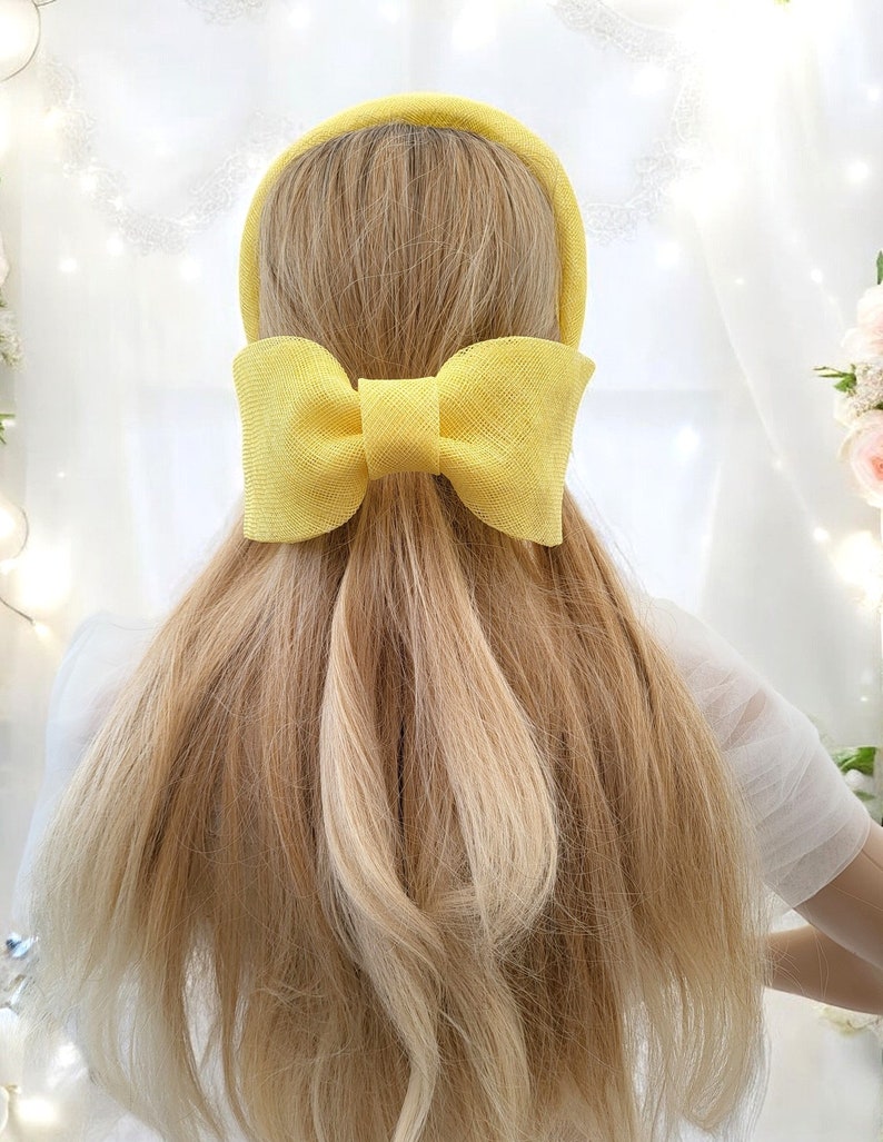 May include: A yellow headband with a large yellow bow. The headband is made of a woven material.