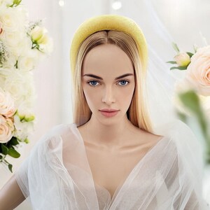May include: A woman with long blonde hair wearing a yellow headband and a white tulle dress. She is standing in front of a white background with flowers.