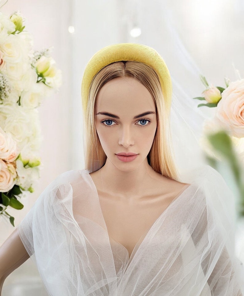 May include: A woman with long blonde hair wearing a yellow headband and a white tulle dress. She is standing in front of a white background with flowers.