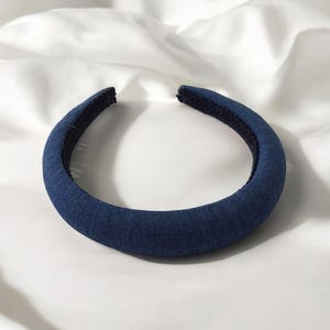 Può includere: Un'ampia fascia per capelli in denim blu scuro. La fascia è realizzata in un materiale morbido e imbottito ed è progettata per essere comoda da indossare.