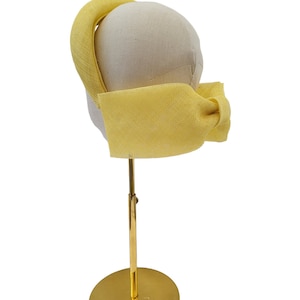 May include: A yellow fabric headband with a bow on a gold stand.
