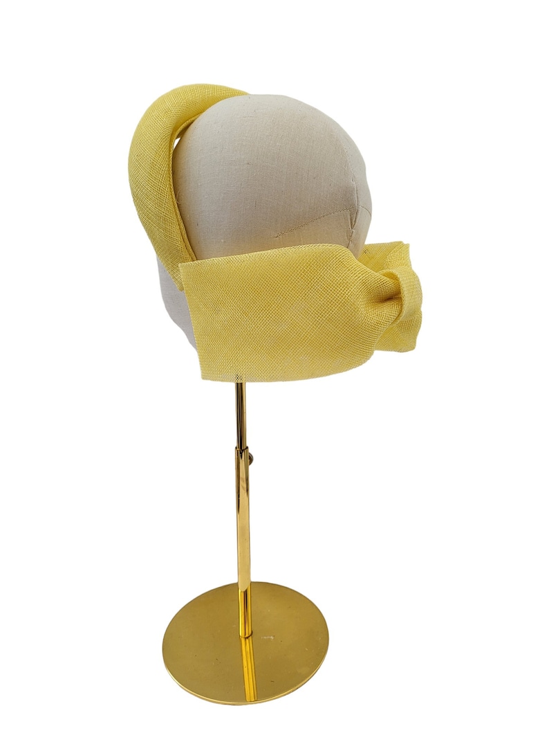 May include: A yellow fabric headband with a bow on a gold stand.