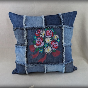 Könnte beinhalten: Ein blaues Jeans-Kissen mit einem floralen Stickmuster. Das Kissen ist aus Patchwork-Jeansstoff mit ausgefransten Kanten.