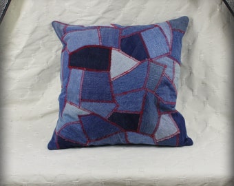May include: A square pillow cover made from patchwork denim fabric. The denim is in various shades of blue and is sewn together with red thread. The pillow cover has a rustic, handmade look.