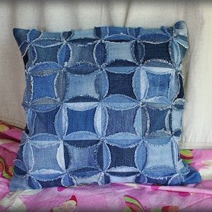 May include: A blue denim cushion with a geometric pattern. The cushion is made from recycled denim and has a frayed edge.