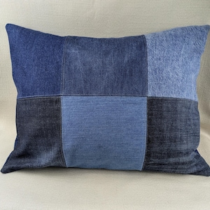 Puede incluir: Una funda de cojín de patchwork hecha de diferentes tonos de tela vaquera azul. La funda de cojín está hecha de seis cuadrados de mezclilla cosidos juntos.