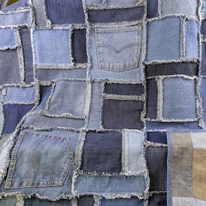 以下が含まれることがあります： 青いデニム生地で作られたパッチワークキルト。キルトは、さまざまなサイズと青色の濃淡の正方形と長方形で構成されています。正方形のいくつかには、ポケットが縫い付けられています。