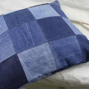 Peut inclure: Un coussin carré en jean avec un motif patchwork. Le coussin est fait de différentes nuances de jean bleu et est cousu ensemble en un motif de grille.