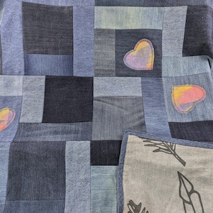 May include: A denim quilt with a patchwork design featuring various shades of blue. The quilt is decorated with colorful hearts and has a gray backing with a leaf design.