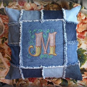 May include: A blue denim pillow with a patchwork design and an embroidered letter "M" in a floral motif.