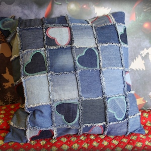 Puede incluir: Una almohada de mezclilla azul con un diseño de patchwork que presenta varios tonos de mezclilla azul y corazones. La almohada está hecha de mezclilla reciclada y tiene un borde deshilachado.