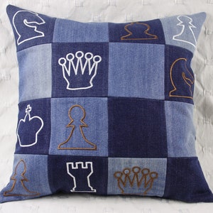 Könnte beinhalten: Ein blaues Jeans-Kissen mit weißen und braunen gestickten Schachfiguren. Das Kissen besteht aus Patchwork-Jeansquadraten.