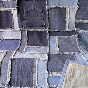 Pode incluir: Uma colcha de retalhos feita de vários quadrados de tecido jeans em diferentes tons de azul. O design apresenta bordas desfiadas entre cada quadrado e inclui bolsos de calças jeans visíveis, exibindo diferentes texturas e lavagens de tecido.