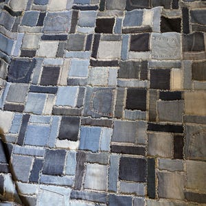 Könnte beinhalten: Eine Patchwork-Decke aus Denim in verschiedenen Blautönen. Die Decke weist ein gitterartiges Muster aus rechteckigen und quadratischen Flicken auf, von denen einige die Taschen der Jeans enthalten. Die Farbpalette umfasst helles, mittleres und dunkles Denimblau.