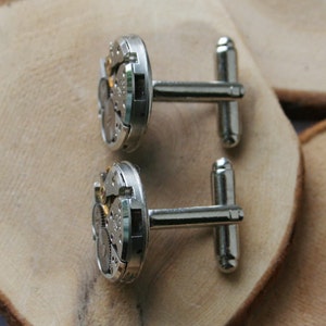 Peut inclure: Une paire de boutons de manchette en argent avec un design circulaire pr&eacute;sentant des engrenages d'horlogerie complexes. Les boutons de manchette ont une finition polie et sont attach&eacute;s &agrave; une barre en argent.