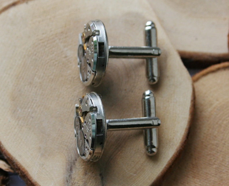 Peut inclure: Une paire de boutons de manchette en argent avec un design circulaire pr&eacute;sentant des engrenages d'horlogerie complexes. Les boutons de manchette ont une finition polie et sont attach&eacute;s &agrave; une barre en argent.