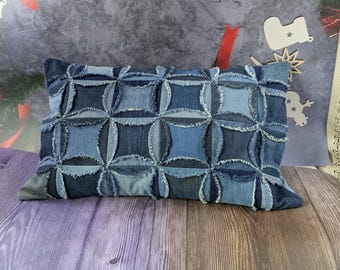 May include: A rectangular denim pillow with a patchwork design. The pillow features a pattern of squares and circles in various shades of blue denim. The edges of the denim pieces are frayed, adding texture to the pillow.
